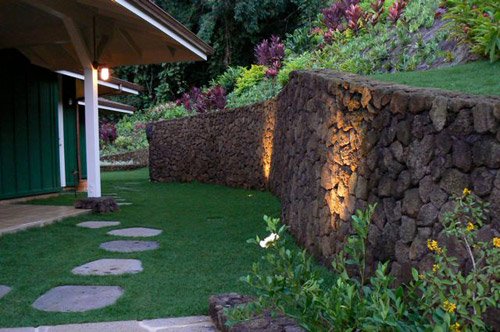 a 110' snaking 'pohaku' (Hawai'ian for 'stone') clad retaining wall curves around the house and holds up the hillside and allowing for a small side yard. Dramatic landscape lighting highlights the sway and bow.