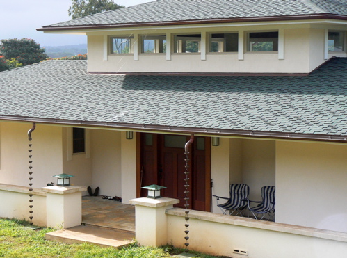 The front entry is a deeply inset and cantilevered portico with custom door and matching sidelights. Instead of downspouts, copper cups on chains guide cascading water into drains below. Above are the 20 360 degree wrapping clerestory windows of the central great room.